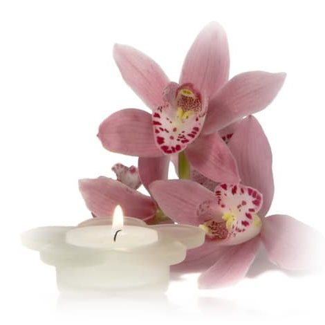 Beautiful pink orchid with white scented candle alight in a pretty petal shaped holder appearing to be reflected in rippling water